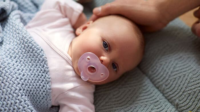 Новорожденный с пустышкой во рту. Использование пустышки помогает ребенку успокоиться и уснуть.